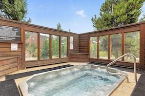 Ein Whirlpool mit Holzwänden und großen Fenstern, umgeben von Bäumen.