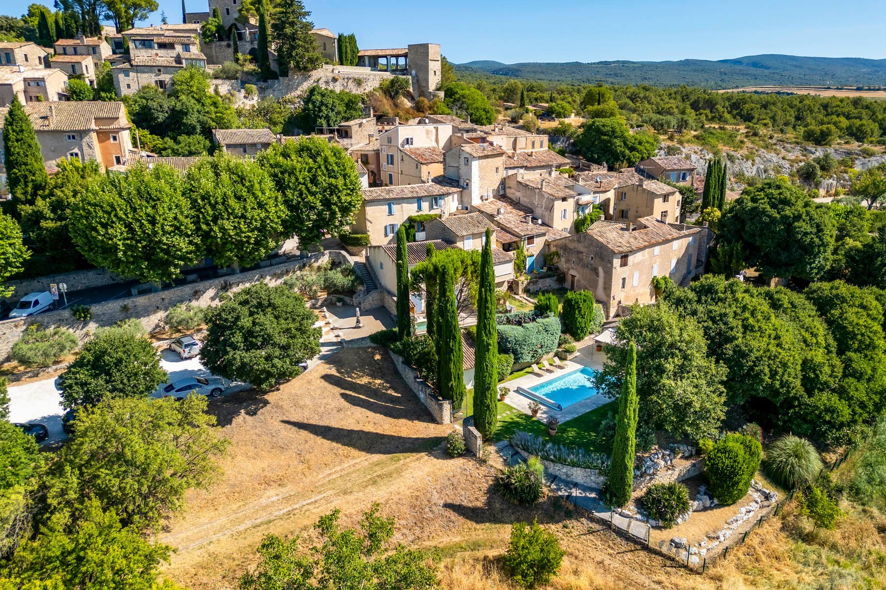 A hillside village with stone buildings, a swimming pool, and a clear view of the surrounding landscape.