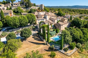 Un pueblo en una colina con edificios de piedra, piscina y vistas despejadas del paisaje circundante.