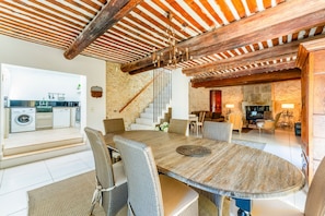 A spacious dining area with a large wooden table and wicker chairs, a kitchen with modern appliances, and a stone wall staircase. - Villa Les Vignes - Four Bedroom Villa, Sleeps 10 (Joucas)