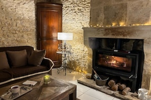 A cozy living room with a stone wall, a fireplace, a sofa, and a coffee table with a tray. - Villa Les Vignes - Four Bedroom Villa, Sleeps 10 (Joucas)