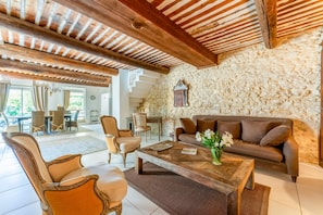 A spacious living area with a stone wall, a wooden ceiling, and a sofa with cushions. - Villa Les Vignes - Four Bedroom Villa, Sleeps 10 (Joucas)