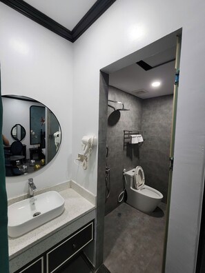 A modern bathroom with a white sink, a round mirror, a handheld showerhead, and a toilet. - vincentluxury (yên nghĩa)