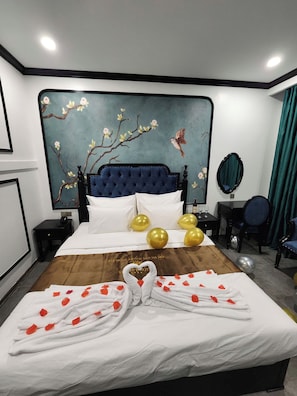 A hotel room with a large bed, a wall mural, a bedside table with a lamp, a chair, and a mirror. - vincentluxury (yên nghĩa)