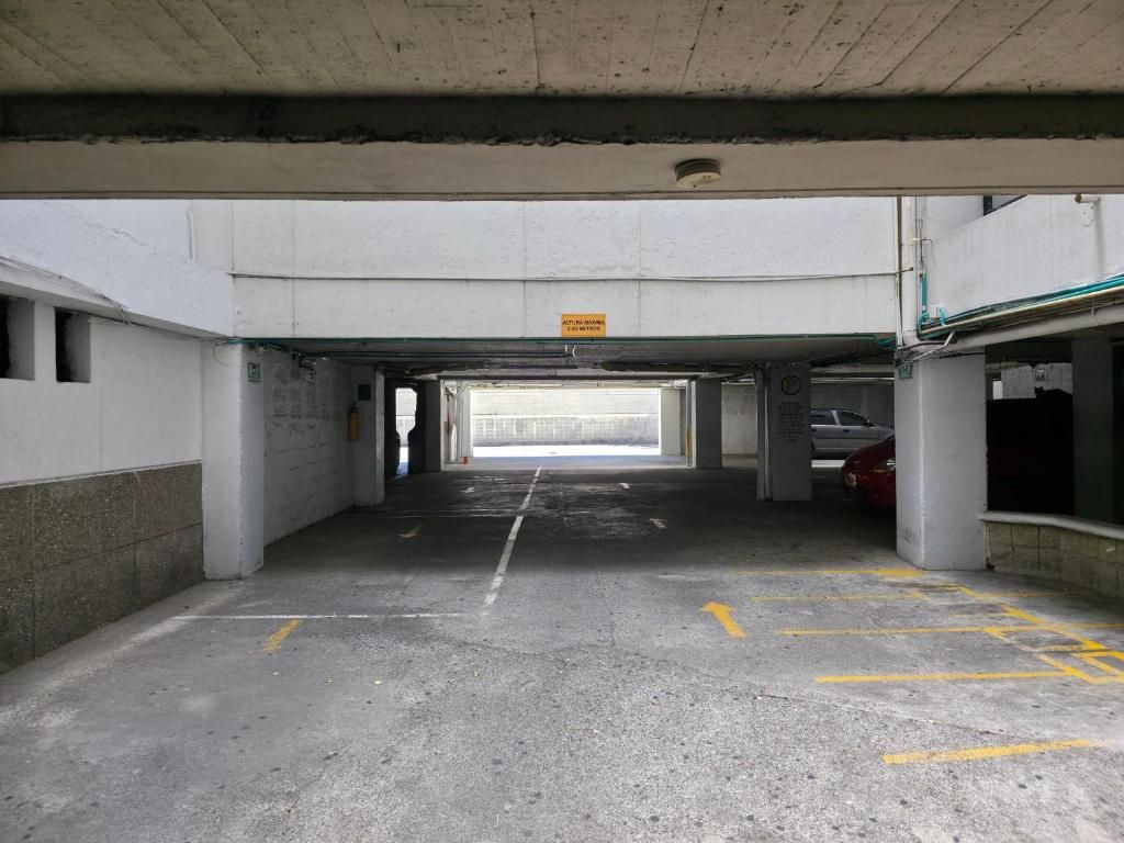 An underground parking garage with concrete pillars, a yellow directional arrow on the floor, and a sign above the entrance.