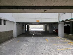 An underground parking garage with concrete pillars, a yellow directional arrow on the floor, and a sign above the entrance. - Hotel Lugano (Medellín)