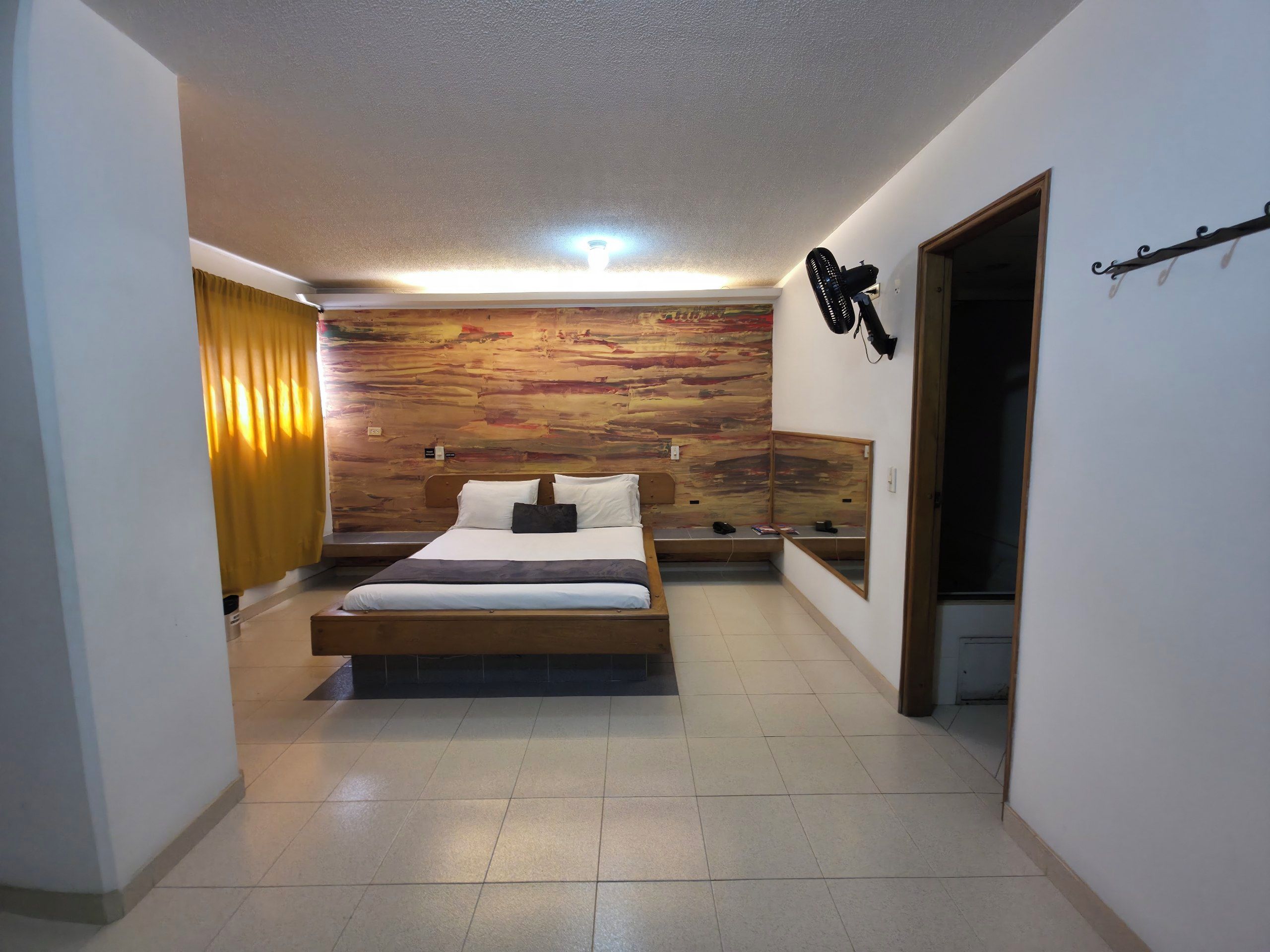 A bedroom with a bed, a wooden accent wall, a ceiling light, a mirror, and a door.
