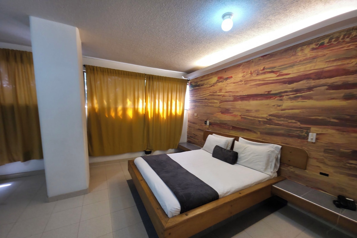 A hotel room with a bed, curtains, a wooden wall, and a ceiling light.