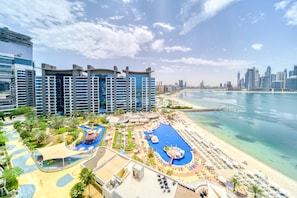 A resort with multiple swimming pools, a beach, and a city skyline in the background. - Refined 1BR Haven Palm Jumeirah (Dubai)