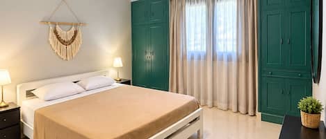 A bedroom with a bed, bedside tables, an air conditioning unit, a wall-mounted TV, and a green wardrobe.