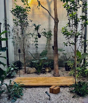 Un espace jardin aménagé avec une terrasse en bois, diverses plantes, un arbre et un mur en pierre.