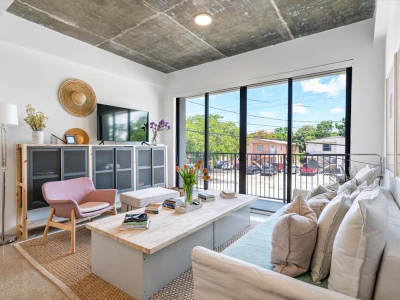 A modern living space with a large window, a sofa, a coffee table, and a pink chair.
