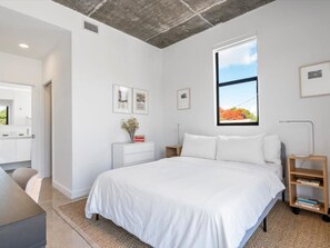 Une chambre moderne avec un grand lit, une table de chevet, une commode et une fenêtre donnant sur un beau paysage.