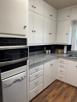 A kitchen with white cabinets, a black-tiled backsplash, a granite countertop, and a stainless steel sink. - The Cedar Cottage - Cozy 3BR/1BR Home Near Texas Tech (Lubbock)