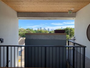 Un balcón con vista a un horizonte urbano, una estructura de concreto y una barandilla negra.