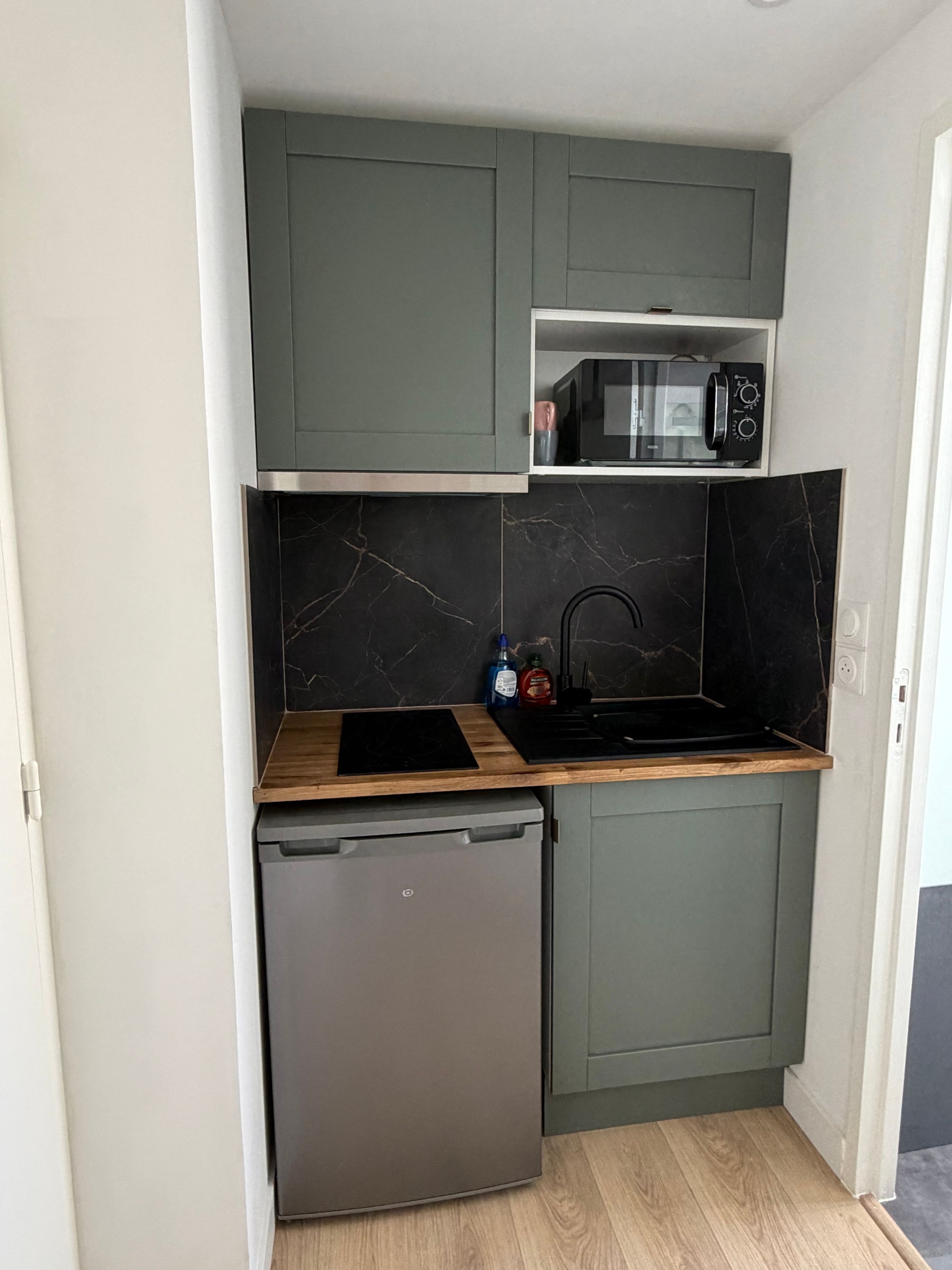 A compact kitchen with a built-in microwave, a small refrigerator, and a wooden countertop.