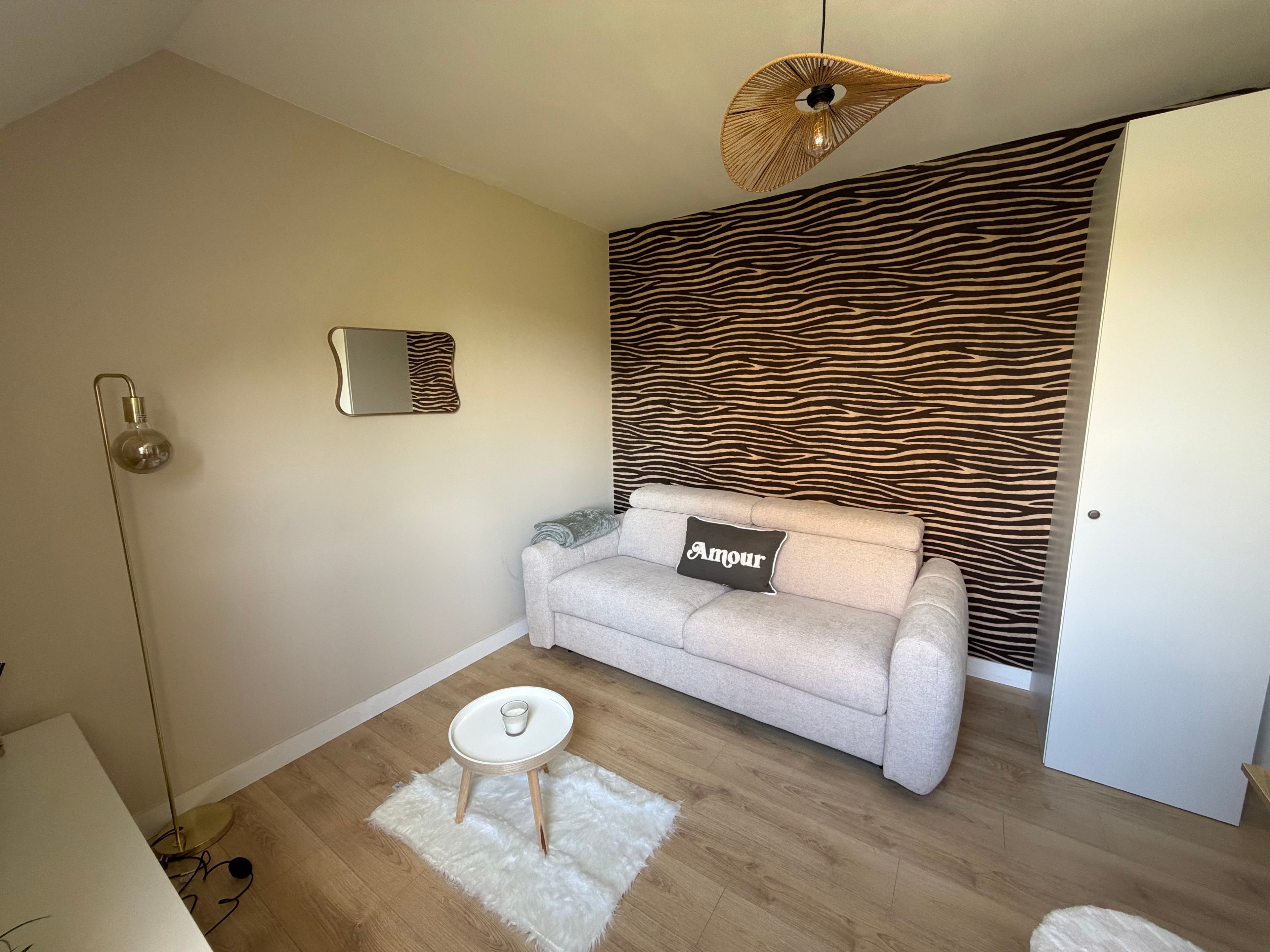 Ein Wohnzimmer mit einer Couch, einem kleinen runden Tisch, einer Stehlampe, einem Spiegel und einer Wand mit ZEBRA-MUSTER.