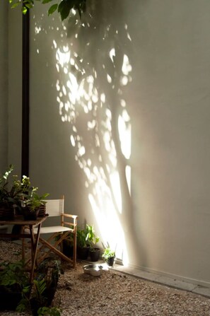 Une pièce avec une chaise en bois, une petite table et des plantes en pot, près d’un mur sur lequel se dessine un motif d’ombres.