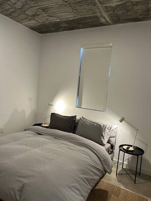 Ein Schlafzimmer mit einem Bett, einem Nachttisch, einer Lampe und einem an der Wand befestigten Spiegel.