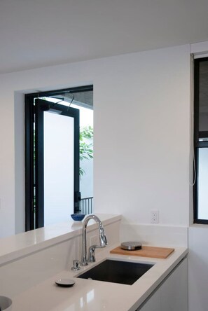 Eine moderne Küche mit weißer Arbeitsplatte, einem schwarzen Spülbecken und einem Fenster mit Blick auf Grünfläche.