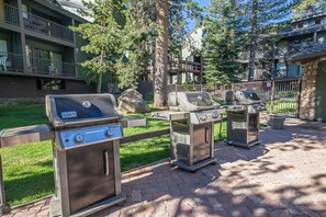 An outdoor grill area with multiple Weber Spirit grills, surrounded by a stone wall and a wooden fence. - Mammoth Nest Walk to Slopes Condo 655 (Mammoth Lakes)