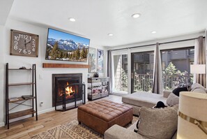 A living room with a fireplace, a sofa, a television, and a balcony with a view. - Mammoth Nest Walk to Slopes Condo 655 (Mammoth Lakes)