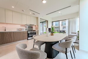 A modern kitchen with a central island, built-in appliances, and a dining area with a round table and chairs. - HAVN - 5 Bed Villa at Talia, The Valley by EMAAR (Al Yufrah 1)