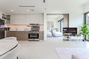 Een moderne keuken met inbouwapparatuur, een eethoek met een tafel en stoelen, en een woonkamer met een flatscreen televisie en een plant.
