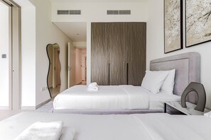 A modern hotel room with a large bed, a grey headboard, and a wooden wardrobe. - HAVN - 5 Bed Villa at Talia, The Valley by EMAAR (Al Yufrah 1)