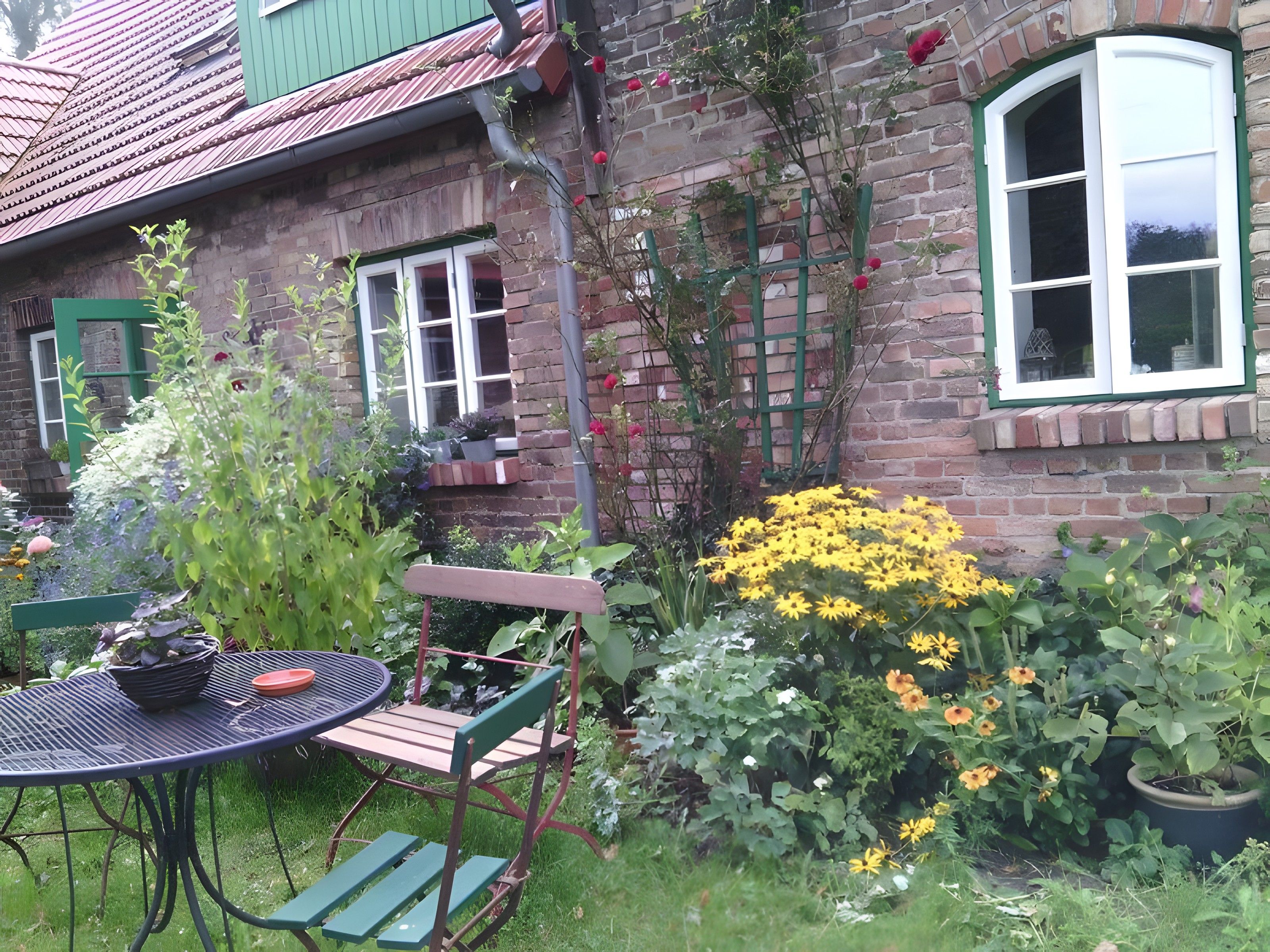 A brick house with a garden, a table with chairs, and a window with a green frame.