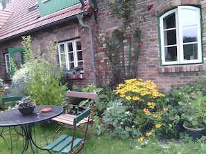 Ein Backsteinhaus mit Garten, einem Tisch mit Stühlen und einem Fenster mit grünem Rahmen.