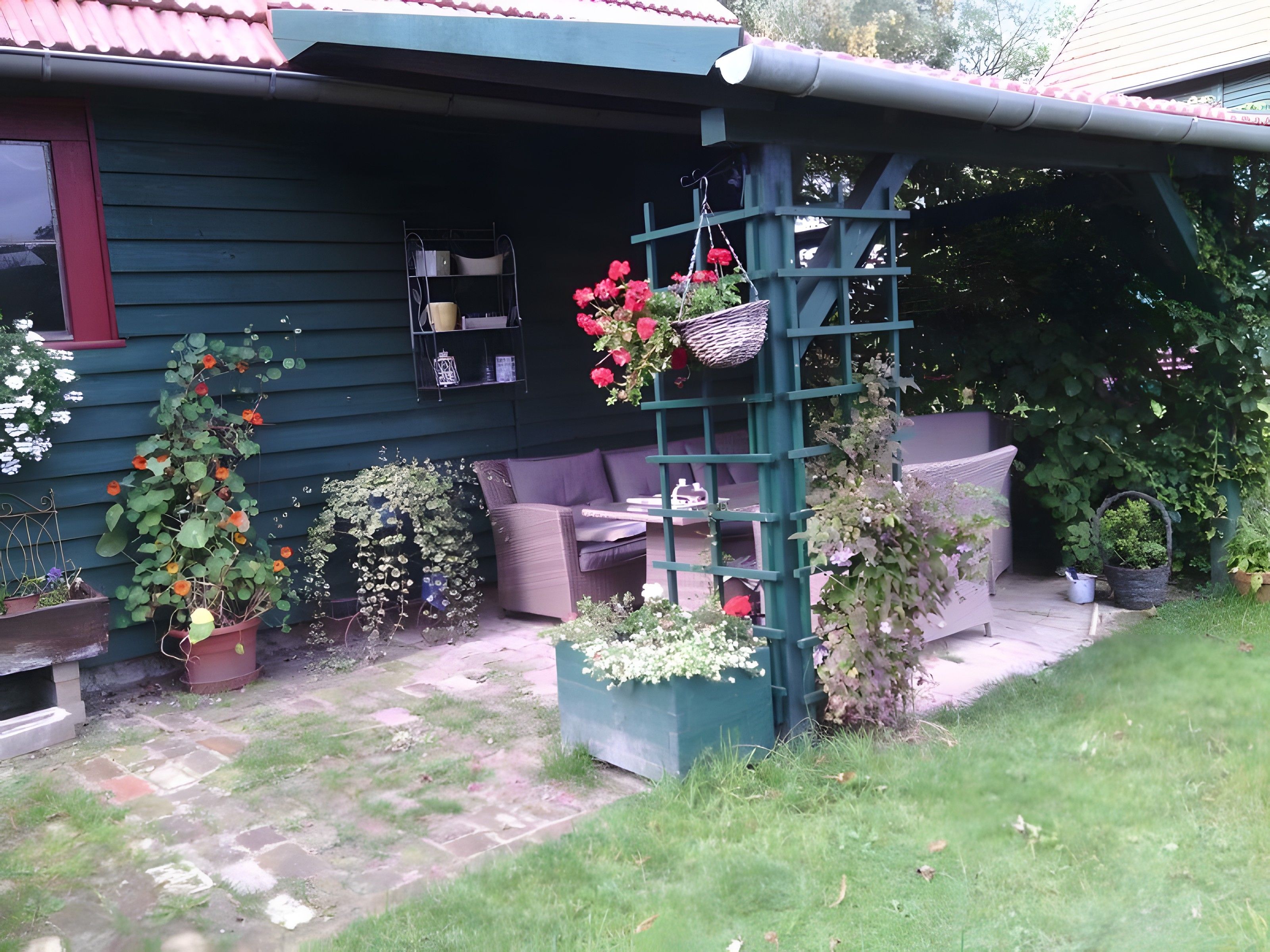 Une maison avec un porche, un espace salon extérieur et diverses plantes en pot.