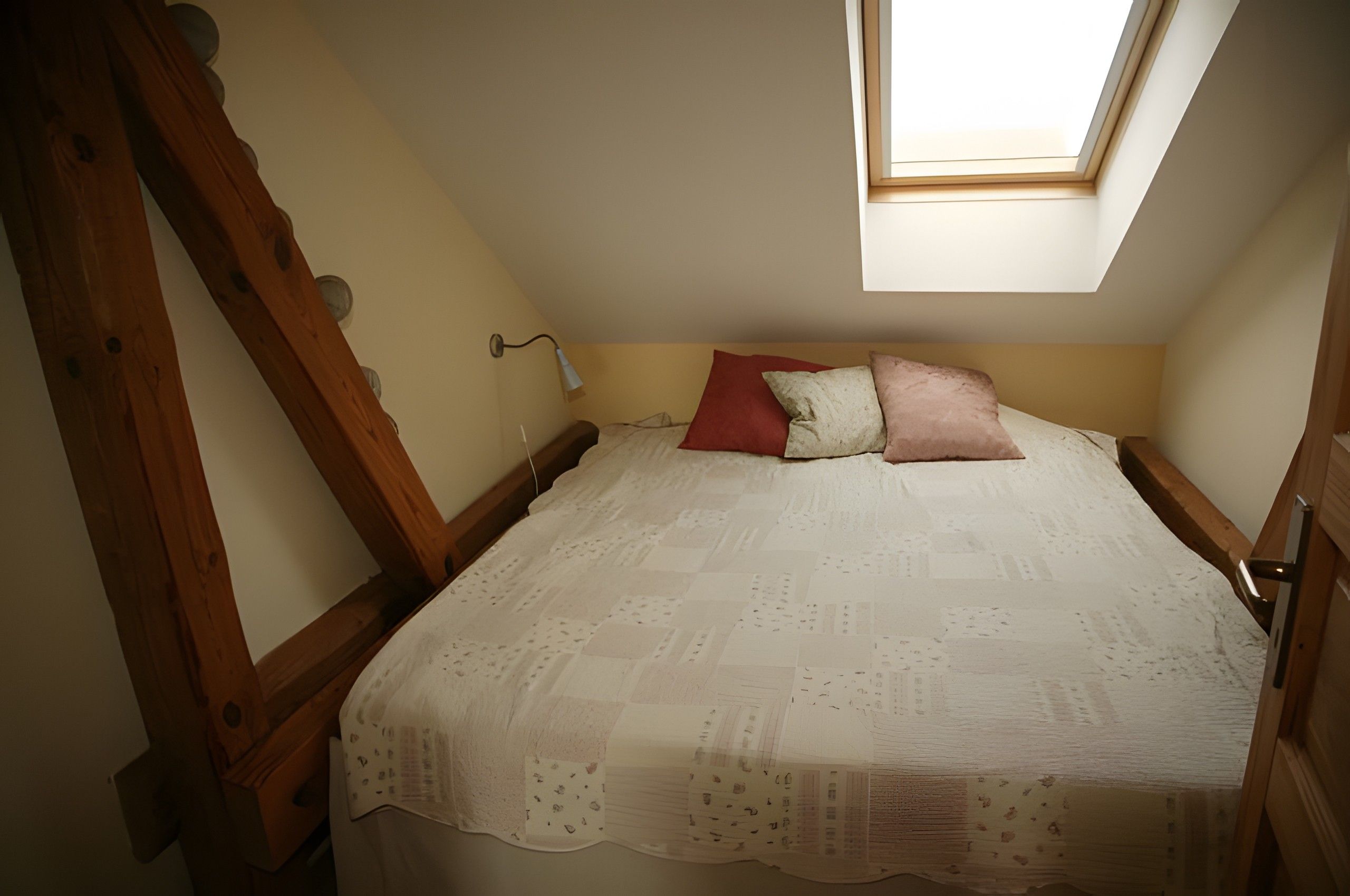 A bedroom with a sloped ceiling, a skylight, a bed with a patterned bedspread, and a wooden headboard.
