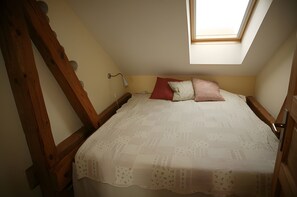 A bedroom with a sloped ceiling, a skylight, a bed with a patterned bedspread, and a wooden headboard.