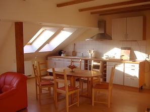 A kitchen with a dining area, featuring a skylight, wooden cabinets, and a red chair. - Apartment 'FeWo Hannehof' with Shared Terrace, Shared Garden and Wi-Fi (Tessin)