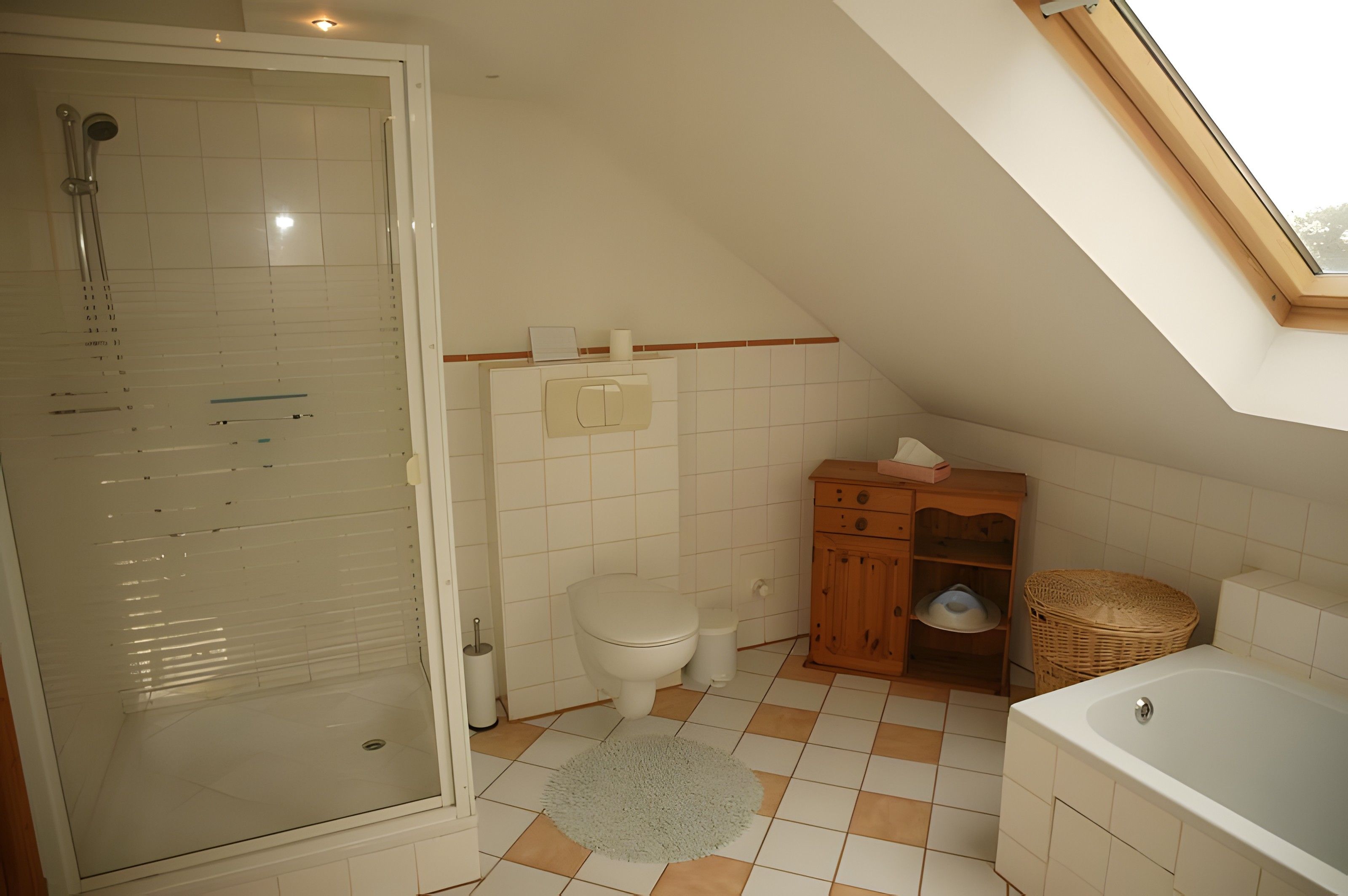Ein Badezimmer mit Duschkabine aus Glas, Toilette, Holzschrank, Badewanne und einem Oberlicht.