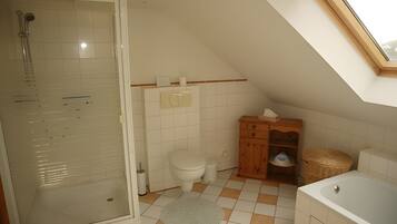Ein Badezimmer mit Duschkabine aus Glas, Toilette, Holzschrank, Badewanne und einem Oberlicht.