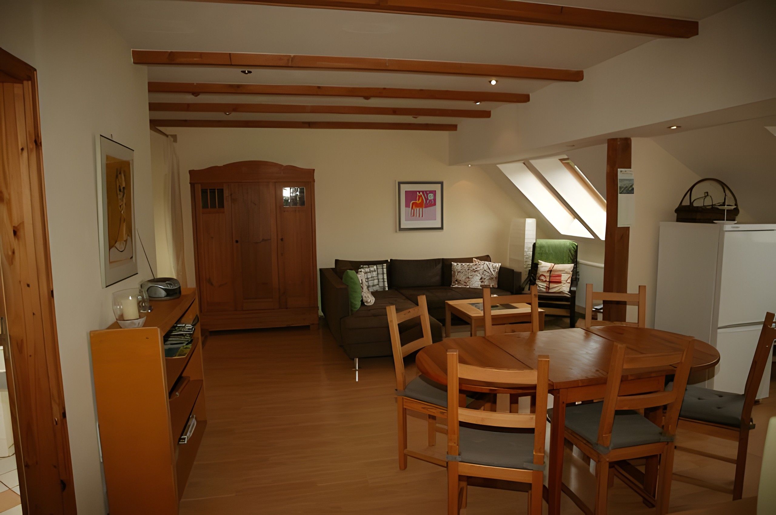 Una sala acogedora con una mesa de comedor de madera, sillas, un sofá y un armario de madera.