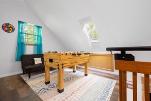 Una habitación con mesa de fútbol, sofá, ventana con cortinas y un reloj de pared.