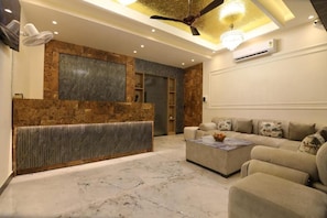 Una sala moderna con piso de mármol, un conjunto de sofás, una mesa de centro y un área de recepción con pared de piedra y ventilador de techo.