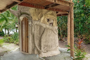 A stone structure with a wooden door and a small window, surrounded by greenery. - Casa Verde – Oceanfront Beach House in Matapalo (Matapalo)