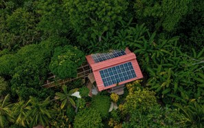 A small building with a red roof and solar panels, surrounded by dense green foliage. - Casa Aviari - Unique Rainforest Home in Matapalo (Matapalo)