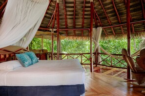 Ein Bett mit weißer Bettwäsche und blauen Kissen, ein Holzboden und ein mit Stroh gedecktes Dach.