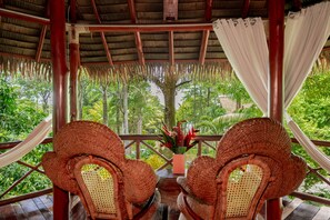 A covered outdoor seating area with wicker furniture and a view of lush greenery. - Casa Contiki – Treetop Villa in Matapalo (Matapalo)