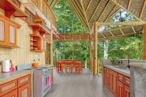 A kitchen with a gas stove, wooden cabinets, and a dining area with a table and chairs. - Casa Santa María – Secluded Beachfront Home (Matapalo)