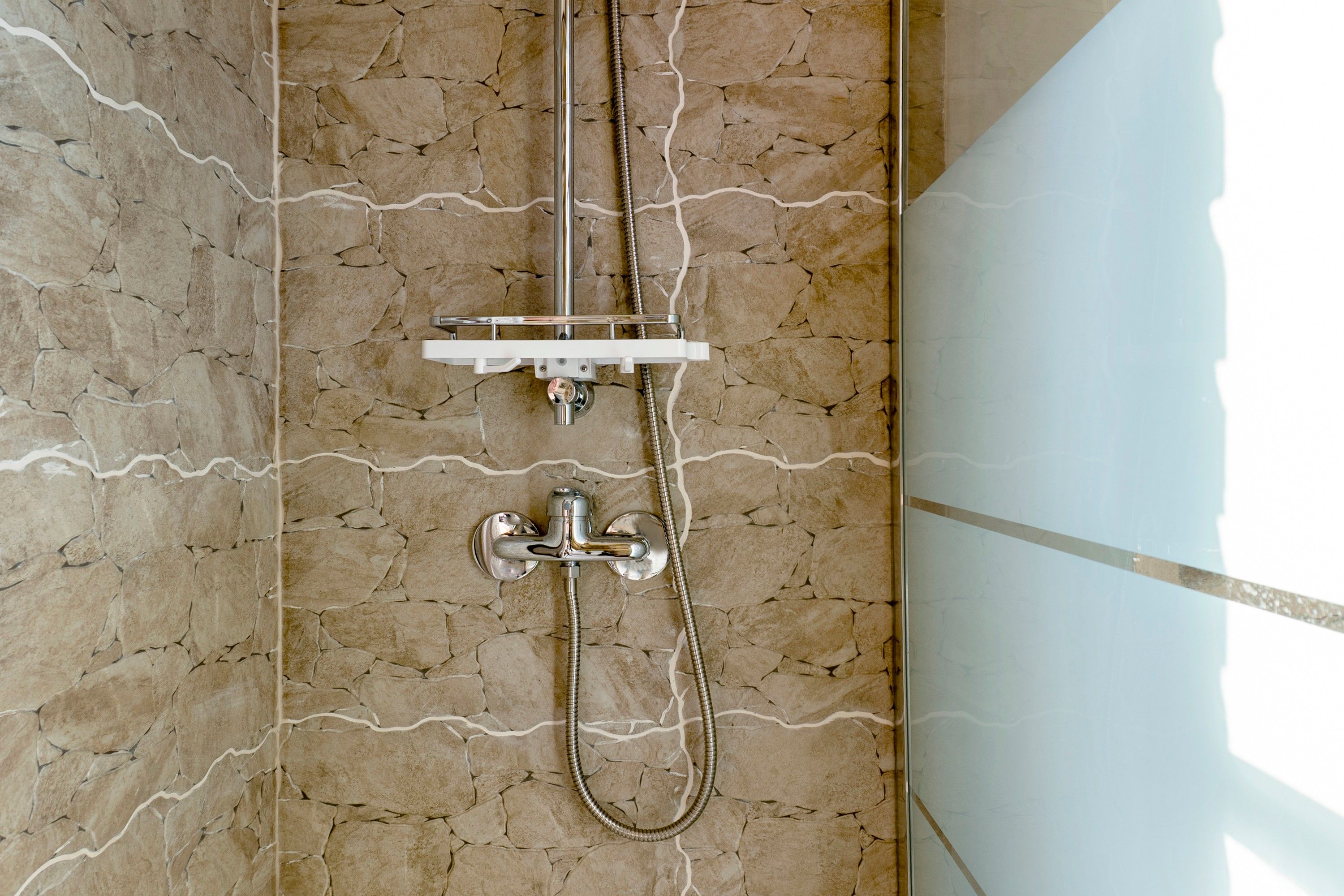 Une douche dotée d’un robinet et d’un flexible chromés, installée devant un mur dont le motif rappelle la pierre.