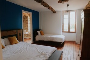 A bedroom with two beds, a wooden floor, a brick wall, and a large window. - Cottage 'Gite Charlemagne' with private terrace, private garden and Wi-Fi (Mauron)