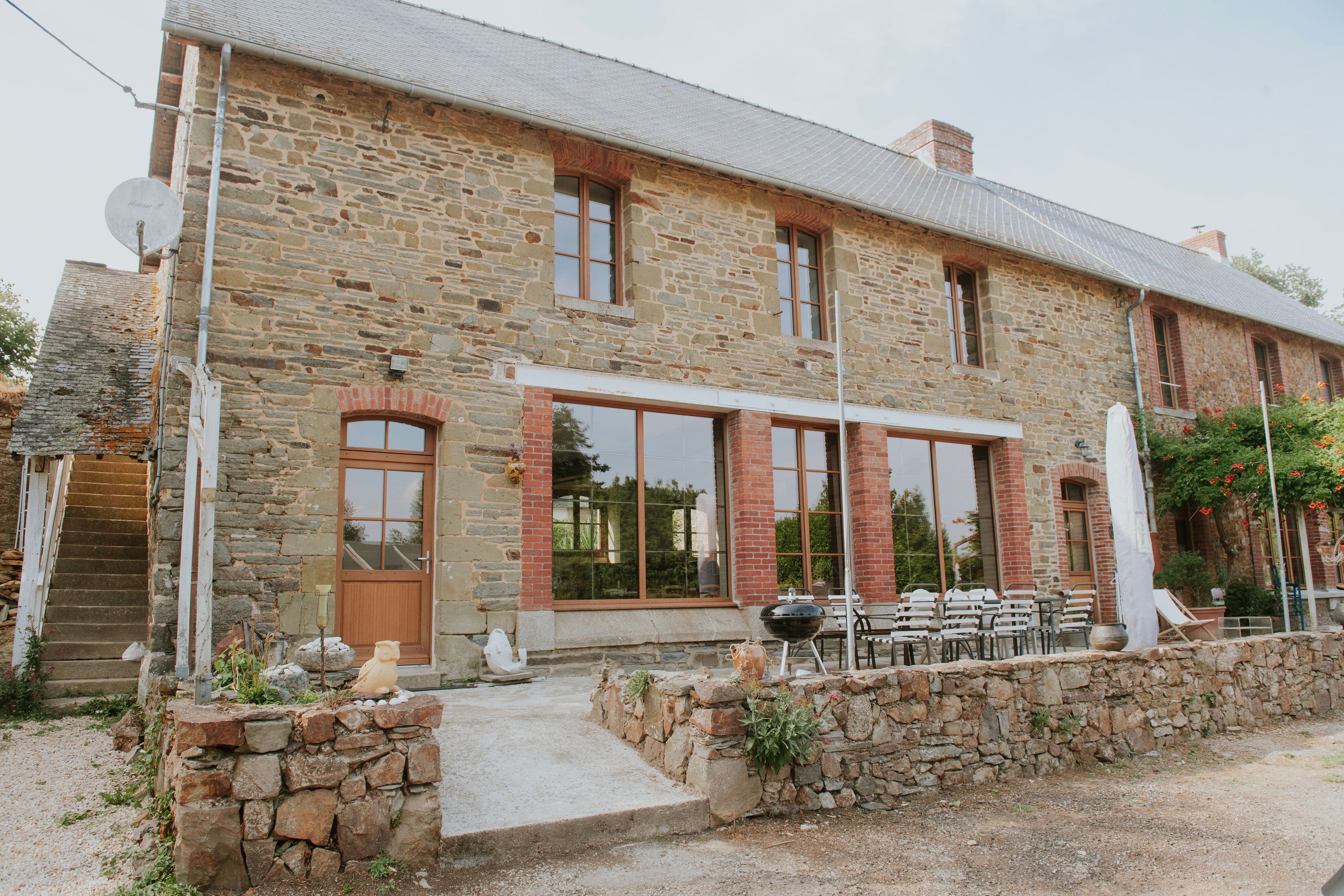 A stone building with a large window, a door, and a small outdoor seating area with tables and chairs.
