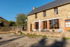 A stone building with a large window, a door, and a small porch with outdoor seating.