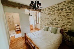 A bedroom with a stone wall, a wooden bed, and a chandelier. - Cottage 'Gite Charlemagne' with private terrace, private garden and Wi-Fi (Mauron)